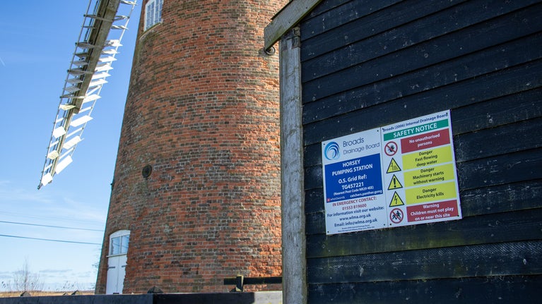 A close up view of the wooden black exterior of the current pumping station with the brickwork of Horsey Windpump visible behind it